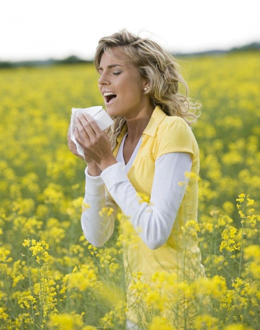 Young woman sneezing in a flowers meadow. Concept: seasonal allergy.