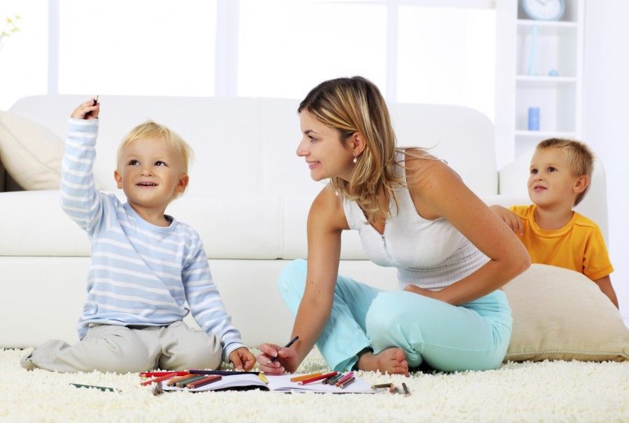 Mother and children sitting on the carpet and drawing with crayons.