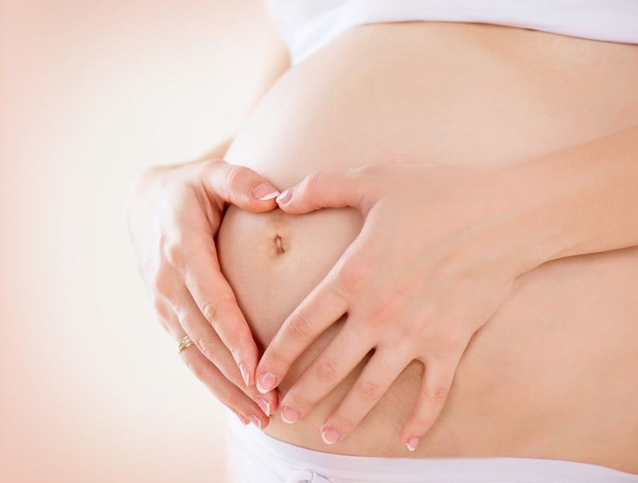 Pregnant Woman holding her hands in a heart shape on her baby bu