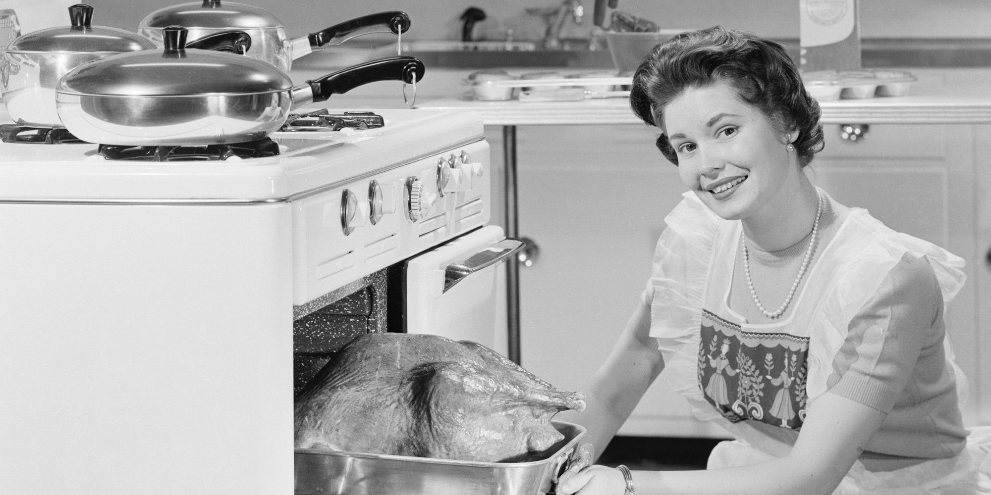 Smiling housewife taking out roasted turkey from cooker and smiling