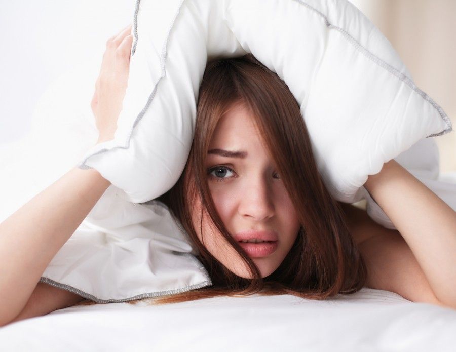 Female lying on bed and closing her ears with pillow