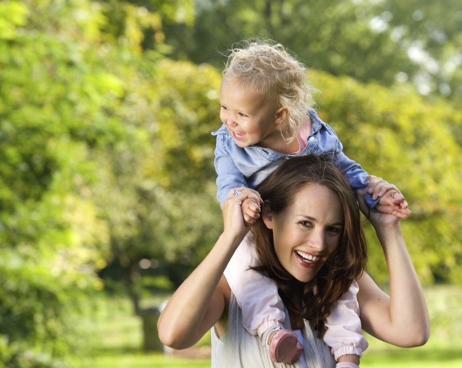 Close up portrait of a smiling mother carrying cute little girl on shoulders