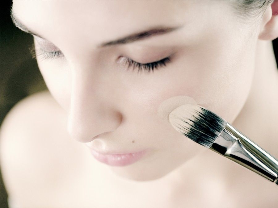 Young woman applying foundation to cheek with make-up brush, close-up