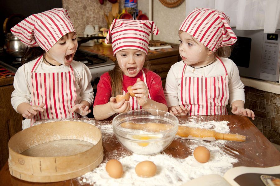 Three little chefs enjoying in the kitchen making big mess. Little girls making bread in the kitchen