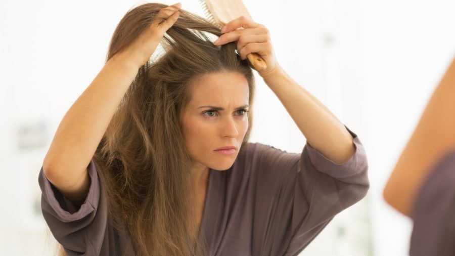 Concerned young woman combing hair in bathroom