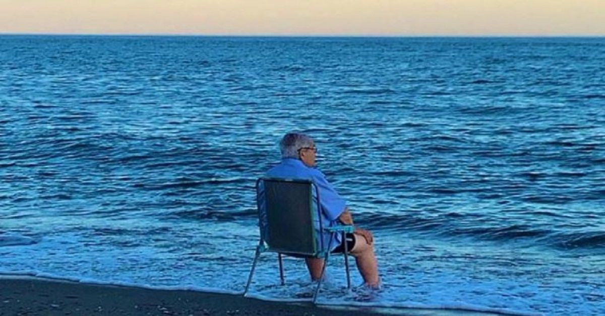 Un vecchio seduto con la sedia di fronte al mare